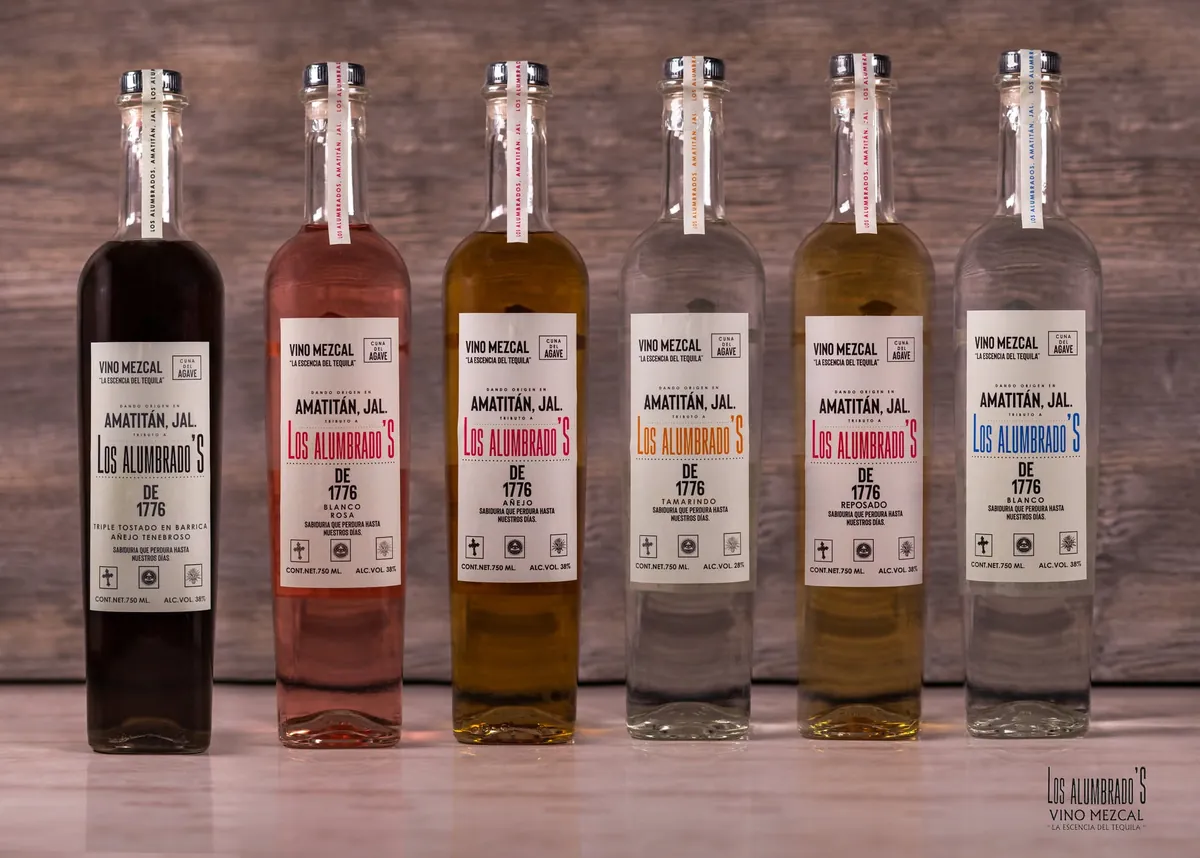 Seis botellas de tequila Los Iluminados en fila sobre una mesa de madera